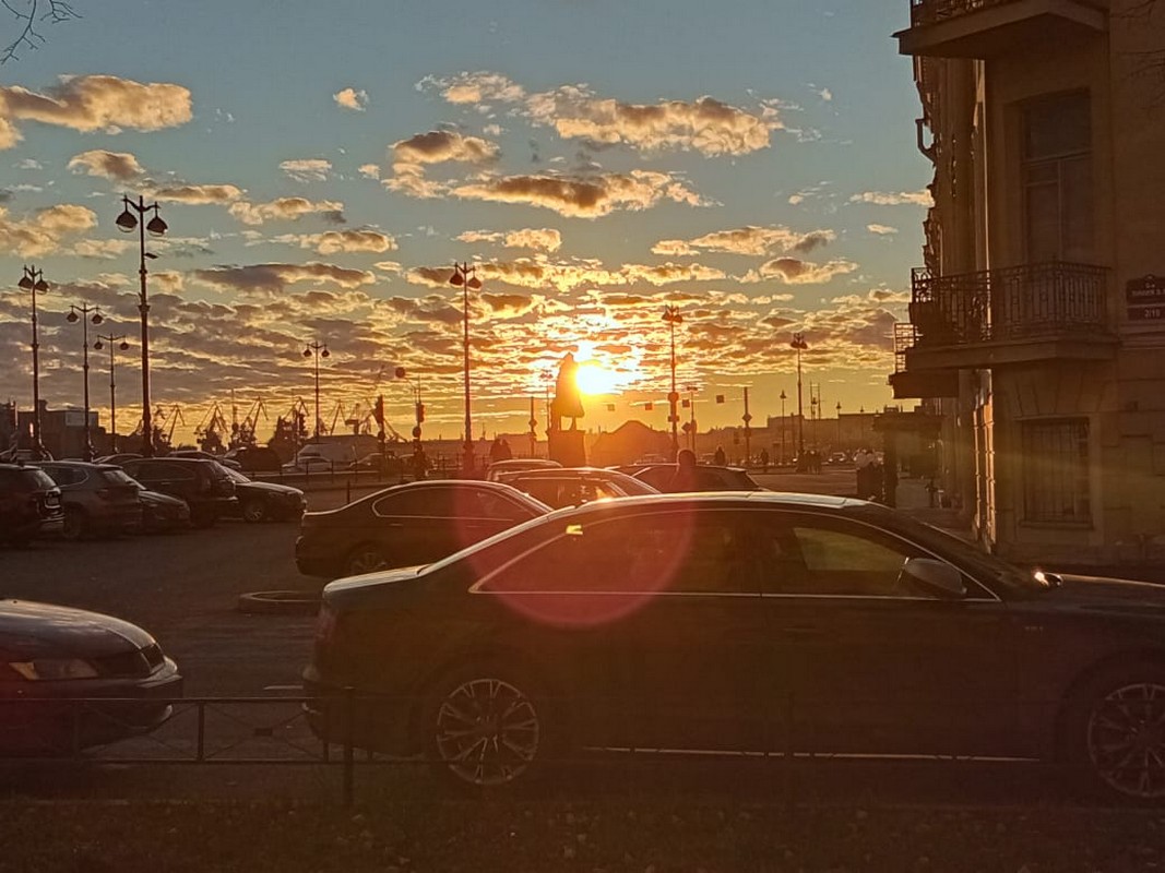 Petersburg, na pierwszym planie parking z autami, ciekawe latarnie, ale widoczne piękne chmury na całym zdjęciu i zachód słońca