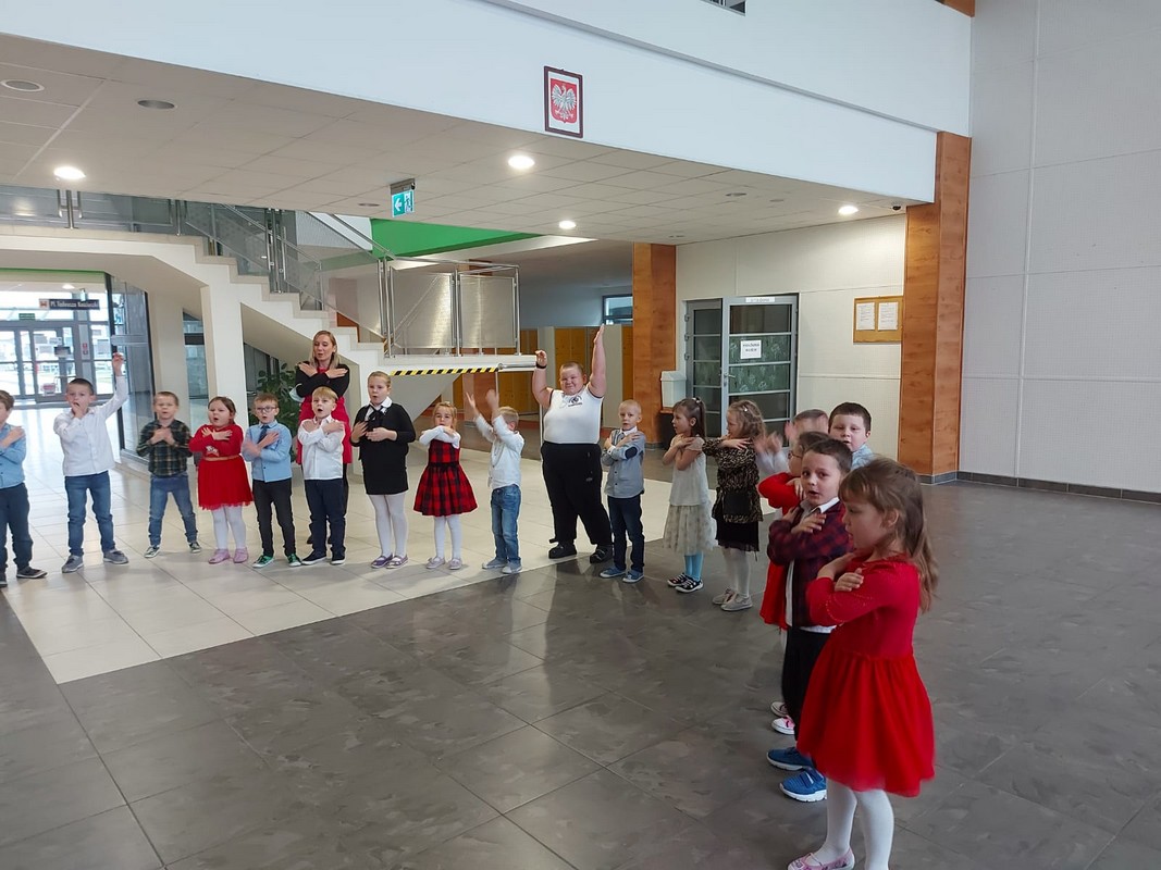 odświętnie ubrane dzieci stoją w kole na holu szkoły - śpiewają kolędę